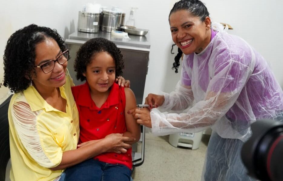 Goiânia e Aparecida antecipam ampliação da vacinação contra gripe - criança no colo da mãe recebendo vacina