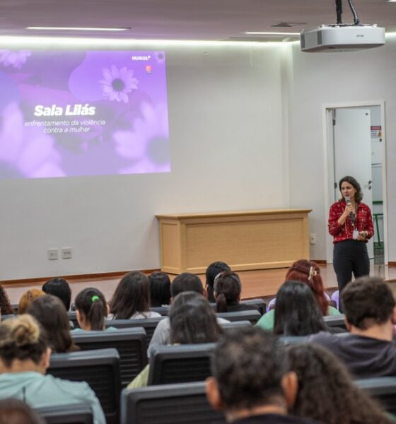 O Hospital Estadual de Urgências Governador Otávio Lage de Siqueira (Hugol) inaugurou, nesta quinta-feira (28/05), sua Sala Lilás, espaço destinado ao acolhimento e apoio de mulheres vítimas de violência. A iniciativa tem como objetivo fortalecer a assistência humanizada e garantir um atendimento mais seguro, reservado e acolhedor às vítimas atendidas. A Sala Lilás foi estruturada para oferecer privacidade, escuta qualificada e suporte durante o atendimento multiprofissional. O ambiente também poderá ser utilizado em atendimentos que que também envolvam crianças e adolescentes em situação de vulnerabilidade. O evento reuniu 168 profissionais do hospital, entre equipes assistenciais, multiprofissionais e setores estratégicos, reforçando a importância da qualificação contínua para o atendimento humanizado e identificação precoce de situações de violência. A inauguração contou com palestra voltada aos profissionais, ministrada pela coordenadora-geral dos Ciclos de Vida e Violências na Superintendência de Políticas e Atenção Integral à Saúde da Secretaria da Saúde de Goiás, Lígia da Fonseca Bernardes. Ela abordou temas relacionados ao enfrentamento da violência contra a mulher, incluindo: fluxo de atendimento dos casos; violência de gênero; Lei Maria da Penha; tipos de violência; ciclo da violência; identificação de sinais de abuso e vulnerabilidade. Capacitção das equipes Segundo Lígia, a capacitação das equipes de saúde é fundamental para garantir acolhimento adequado às vítimas. “Os profissionais da saúde têm papel essencial na identificação precoce dos sinais de violência e no acolhimento humanizado dessas mulheres”. “Muitas vezes, o hospital é a primeira porta de apoio procurada pela vítima, e estar preparado para esse atendimento pode fazer toda a diferença no rompimento do ciclo da violência”, destacou. Sala Lilás – avanço no cuidado De acordo com a supervisora multiprofissional do Hugol, Gabriela Vieira, a implantação da Sala Lilás representa um avanço importante no cuidado às vítimas em situação de vulnerabilidade. “A criação desse espaço fortalece o acolhimento humanizado dentro da unidade e proporciona mais segurança, privacidade e suporte emocional às pacientes atendidas. É um ambiente pensado para oferecer escuta qualificada e assistência integral”, afirmou. A criação da Sala Lilás integra as ações de fortalecimento das políticas de proteção e cuidado às vítimas de violência desenvolvidas pelo Hugol, promovendo um ambiente mais acolhedor e preparado para assistência integral aos pacientes em situação de vulnerabilidade. Além do acolhimento imediato, o espaço também busca contribuir para o encaminhamento adequado das vítimas à rede de apoio e proteção, fortalecendo o trabalho integrado entre saúde, assistência social e segurança pública. Saiba mais Sala Lilás do Hugol vai acolher mulheres vítimas de violência