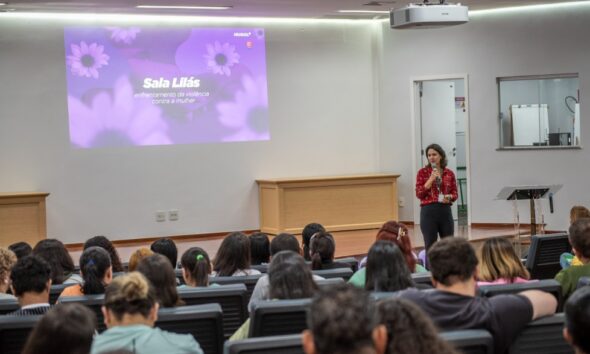 O Hospital Estadual de Urgências Governador Otávio Lage de Siqueira (Hugol) inaugurou, nesta quinta-feira (28/05), sua Sala Lilás, espaço destinado ao acolhimento e apoio de mulheres vítimas de violência. A iniciativa tem como objetivo fortalecer a assistência humanizada e garantir um atendimento mais seguro, reservado e acolhedor às vítimas atendidas. A Sala Lilás foi estruturada para oferecer privacidade, escuta qualificada e suporte durante o atendimento multiprofissional. O ambiente também poderá ser utilizado em atendimentos que que também envolvam crianças e adolescentes em situação de vulnerabilidade. O evento reuniu 168 profissionais do hospital, entre equipes assistenciais, multiprofissionais e setores estratégicos, reforçando a importância da qualificação contínua para o atendimento humanizado e identificação precoce de situações de violência. A inauguração contou com palestra voltada aos profissionais, ministrada pela coordenadora-geral dos Ciclos de Vida e Violências na Superintendência de Políticas e Atenção Integral à Saúde da Secretaria da Saúde de Goiás, Lígia da Fonseca Bernardes. Ela abordou temas relacionados ao enfrentamento da violência contra a mulher, incluindo: fluxo de atendimento dos casos; violência de gênero; Lei Maria da Penha; tipos de violência; ciclo da violência; identificação de sinais de abuso e vulnerabilidade. Capacitção das equipes Segundo Lígia, a capacitação das equipes de saúde é fundamental para garantir acolhimento adequado às vítimas. “Os profissionais da saúde têm papel essencial na identificação precoce dos sinais de violência e no acolhimento humanizado dessas mulheres”. “Muitas vezes, o hospital é a primeira porta de apoio procurada pela vítima, e estar preparado para esse atendimento pode fazer toda a diferença no rompimento do ciclo da violência”, destacou. Sala Lilás – avanço no cuidado De acordo com a supervisora multiprofissional do Hugol, Gabriela Vieira, a implantação da Sala Lilás representa um avanço importante no cuidado às vítimas em situação de vulnerabilidade. “A criação desse espaço fortalece o acolhimento humanizado dentro da unidade e proporciona mais segurança, privacidade e suporte emocional às pacientes atendidas. É um ambiente pensado para oferecer escuta qualificada e assistência integral”, afirmou. A criação da Sala Lilás integra as ações de fortalecimento das políticas de proteção e cuidado às vítimas de violência desenvolvidas pelo Hugol, promovendo um ambiente mais acolhedor e preparado para assistência integral aos pacientes em situação de vulnerabilidade. Além do acolhimento imediato, o espaço também busca contribuir para o encaminhamento adequado das vítimas à rede de apoio e proteção, fortalecendo o trabalho integrado entre saúde, assistência social e segurança pública. Saiba mais Sala Lilás do Hugol vai acolher mulheres vítimas de violência
