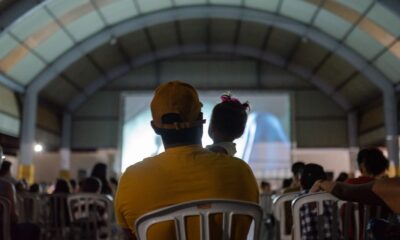 Governo de Goiás leva Cine Leitura do Bem a mais quatro municípios - público assistindo a sessão de cinema do projeto. Em primeiro plano, pai com bebê nos braços assistindo ao filme