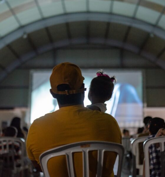 Governo de Goiás leva Cine Leitura do Bem a mais quatro municípios - público assistindo a sessão de cinema do projeto. Em primeiro plano, pai com bebê nos braços assistindo ao filme